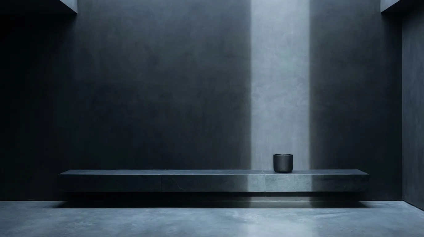 Stealth wealth interior with a black concrete candle on a slate console, charcoal walls and cool directional light