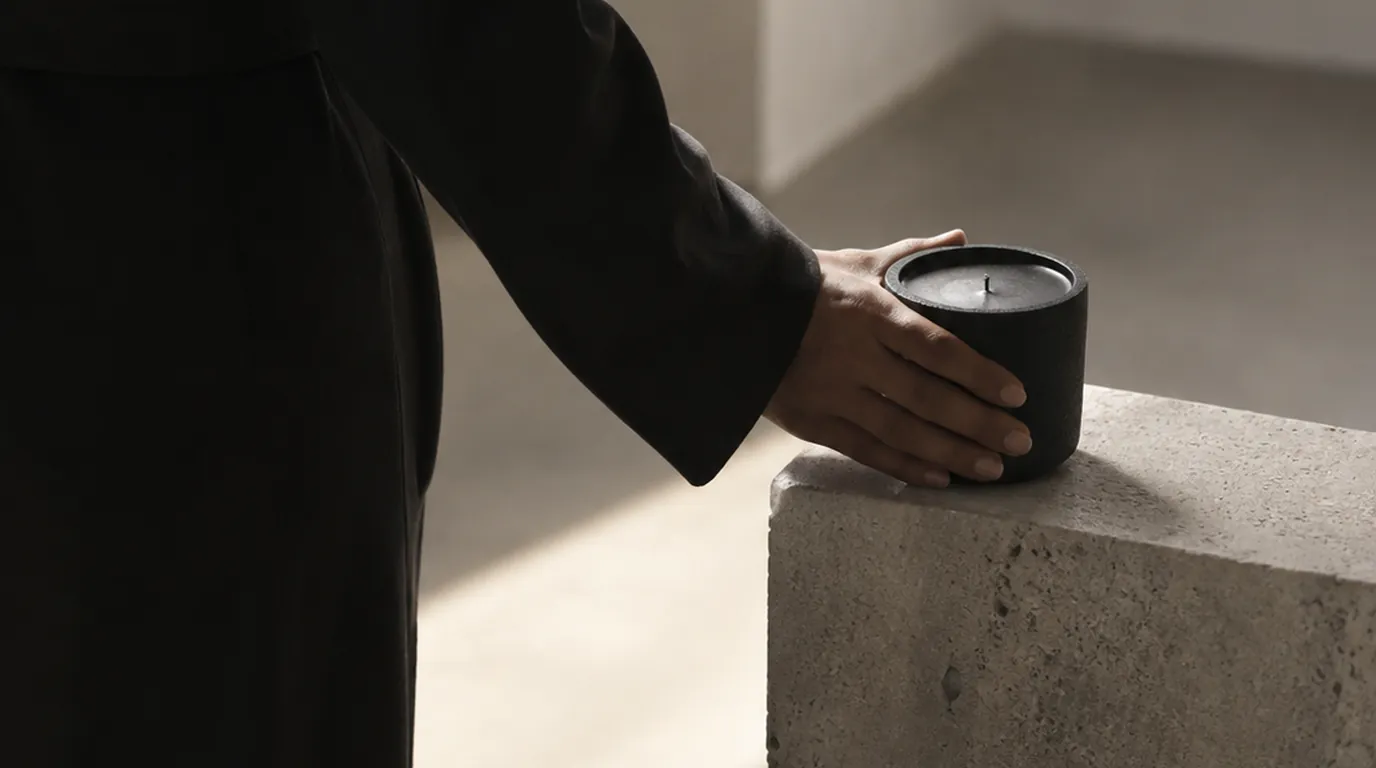 Black concrete candle isolated in a pool of cool light on a graphite plinth in a dark gallery space